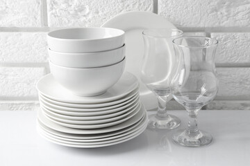 Different clean dishware on white table near brick wall