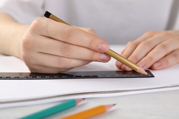 Woman drawing sketch with ruler and pencil on notebook at light table, closeup