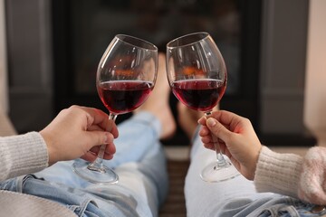 Couple with glasses of wine near fireplace on floor at home, selective focus