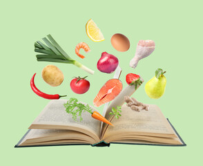 Fresh ingredients in air over recipe book on light green background