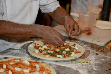 Chef preparing handmade pizza by placing toppings on raw dough in a professional kitchen