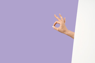Female hand showing OK with blank poster on lilac background