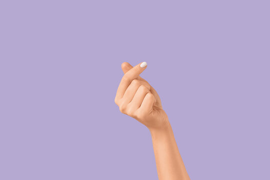 Female hand making heart gesture on lilac background