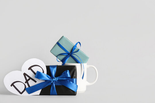 Cup with gift boxes and word DAD on grey background. Father's day celebration
