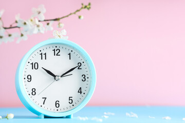 Alarm clock and blooming branch on pink background. Spring time