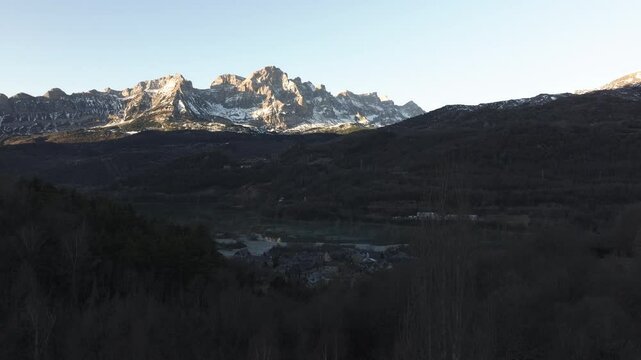 Aerial shot - Sunlight illuminating the snowy peaks of Pena Ubina, casting long shadows across the picturesque valley of Lena and the charming municipality of Quiros in Asturias, Spain