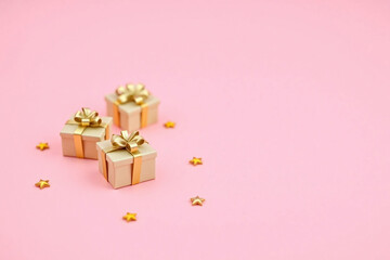 three gift boxes with gold bows and ribbons on a pink background