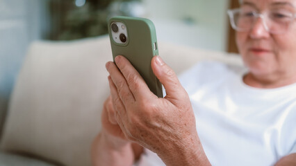 Close-up of a senior womans hand holding a smartphone and moving her finger across the screen. She is texting on her mobile and scrolling through her social media feed. Technology and retirees.