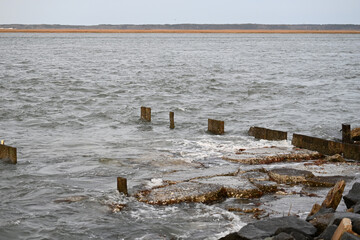 Old worn pier dock wood pillars in a stormy sea with waves breaking over rocks 