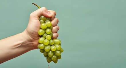 Hand squeezing fresh green grapes against green background