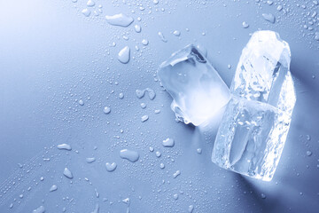 Pieces of clear ice and water drops on light blue table, top view. Space for text