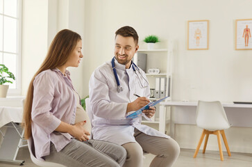 Young pregnant woman visiting doctor in clinic, male medical gynecologist consulting expectant...