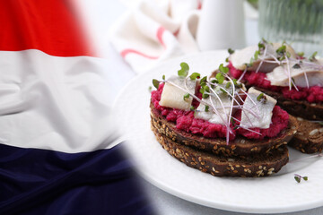 Tasty sandwiches with herring on wooden table and flag of Netherlands