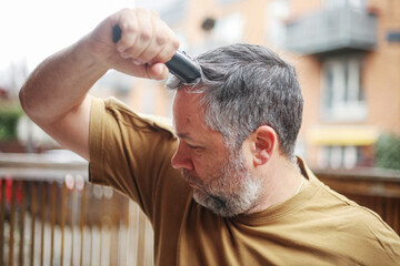 Obraz premium Self-grooming at home: man shaving head with trimmer in casual clothes