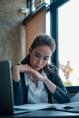 Professional woman in office attire deeply focused on reviewing documents by a window, showcasing...