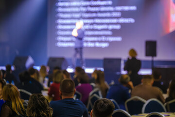 Audience attending a speaker presentation at a professional conference on a stage with lighting.
