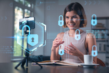 Happy woman is making video blog using smartphone on a tripod explaining with hands at office workplace. Concept of online stream, business education, conference call. Lock icons hologram