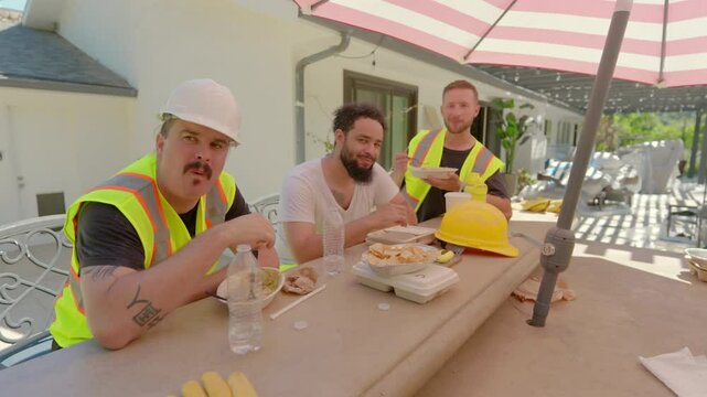 In a bright and sunny outdoor setting, three construction workers are taking a welldeserved break, enjoying their meals and refreshments together while embracing the joy of leisure and camaraderie