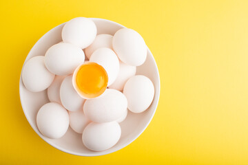 Bowl of organic eggs top view. Pile of raw chicken eggs isolated on yellow background. Yolk in eggshell flatlay. Easter. High quality photo.