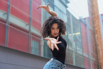 African American woman dancing in a creative pose between benches in an urban setting. She wears casual clothes and shows balance, strength, and expression. Concept of movement, art, and freedom. 