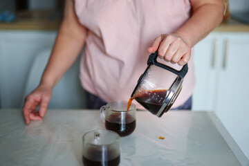 clouse up hands of Middle-aged woman pouring coffee in a cozy home kitchen