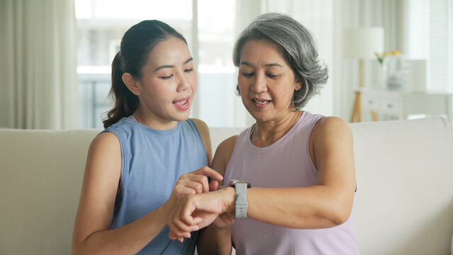 Young adult child give gift AI smart watch IOT app to mature middle age old mum. Love health care older mom asia elder people sit at home sofa happy family wear wrist trace help protect aging life.