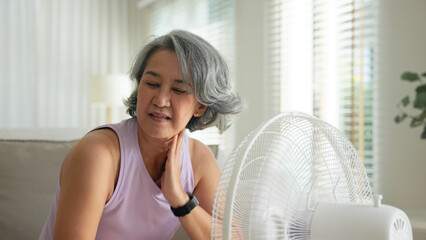 Asia adult people middle age old woman sit at sofa home feel hot flash fever use fan waving hand...