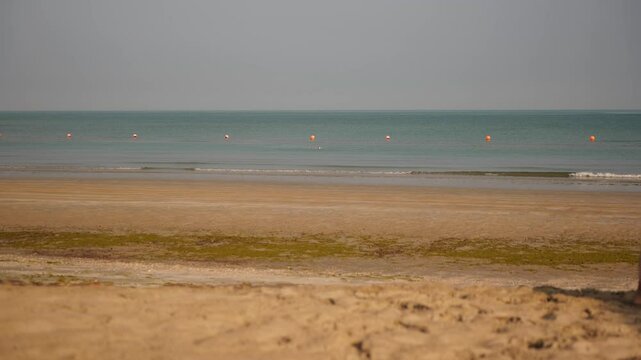 A woman departs from the beach, holding a towel as she steps through the sand. The quiet ocean and open sky evoke a sense of peace and closure
