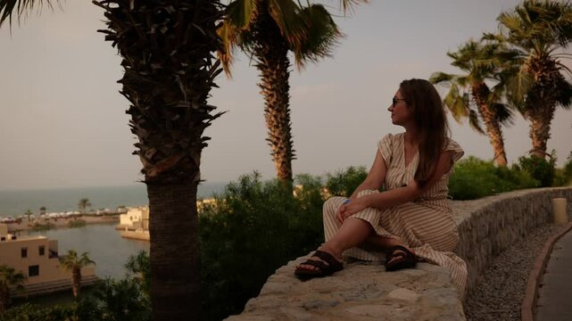 A thoughtful woman enjoys the serene beauty of the sea while surrounded by palm trees