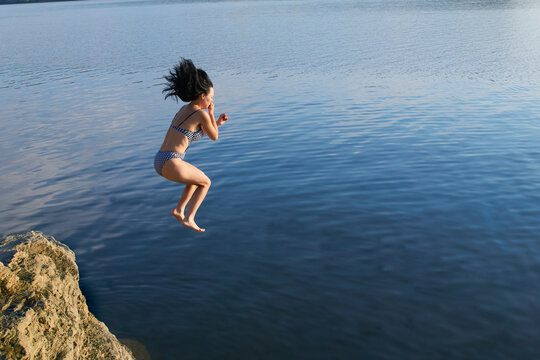 Young girl in a swimsuit jumping from a cliff into the sea water