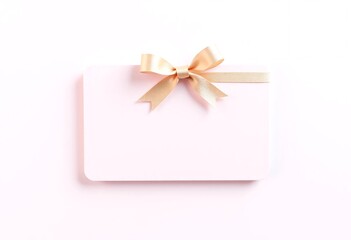A Pastel Pink Gift Box with a Gold Ribbon Bow. A minimalist flat lay of a blank light pink gift box or card adorned with a delicate gold ribbon bow