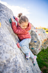 Little girl climbing an artificial climbing wall in a playground, developing strength and...