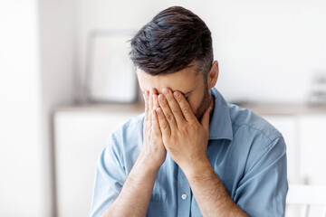 Fatigue From Work. Stressed male entrepreneur covering face with hands at workplace, tired after using laptop, having business problems, overworked businessman feeling unhappy and unwell, free space