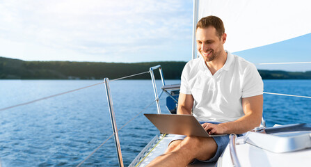 Happy Man On Yacht Sitting With Laptop Working Living On Sailboat During Summer. Liveaboard Tour....
