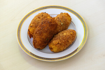 Tasty homemade dimer chop on a white plate, set against a light wooden surface. This delicious dish, also known as egg chop or dimer alur chop, is a very popular snack in Bangladeshi cuisine.