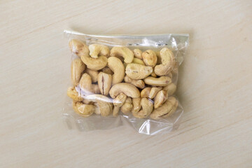 From a top view, a packet of cashew nuts rests on a light wooden surface. The scientific name for these nuts is Anacardium occidentale.