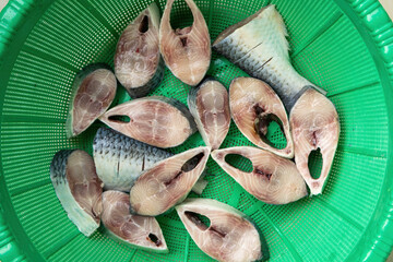 Slices of fresh, raw Hilsa fish (Tenualosa ilisha) in a green basket are ready for cooking. This world-famous Ilish fish from the Padma River in Bangladesh is also popular in West Bengal, India.