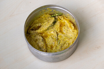 Delicious shorshe ilish on silverware on a light wooden surface. This popular Bengali dish, made with Hilsa fish (Tenualosa ilisha), is cooked with mustard seed.