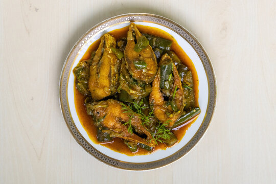 A popular Bengali food, this delicious brinjal curry features hilsa fish (Tenualosa ilisha) and is served on a ceramic plate set on a light wooden surface. Top view.