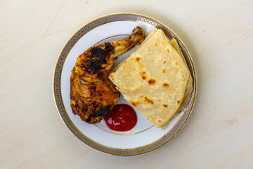 Homemade delicious grilled barbecue chicken, served with cut pieces of Paratha and tomato sauce on a ceramic plate. A very tasty and nutritious Bengali-style roasted chicken. Top view.