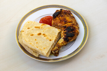 Homemade delicious grilled barbecue chicken with cut pieces of Paratha and tomato sauce served on a ceramic plate on a wooden background. Tasty Bengali-style roasted chicken, a nutritious food.