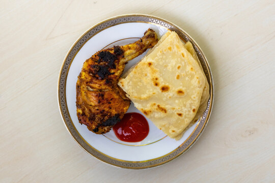 Homemade delicious grilled barbecue chicken, served with cut pieces of Paratha and tomato sauce on a ceramic plate. A very tasty and nutritious Bengali-style roasted chicken. Top view.