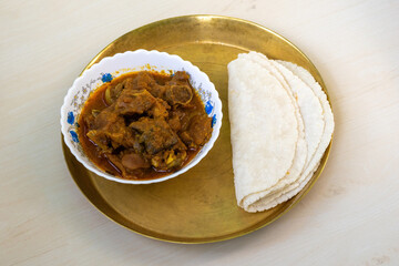 Tasty mutton curry and roti (flatbread) served on a brass plate on a light wooden surface. A very delicious Bengali meal.