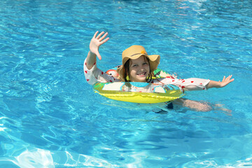 Smiling little girl in a straw hat in swimming pool on summer vacation. Children's, family summer vacation.