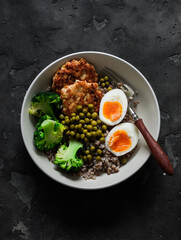 Balanced lunch - buckwheat, broccoli, chopped chicken cutlets, boiled egg on a dark background, top view