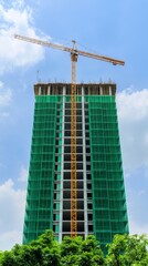 Fototapeta premium Construction Site to Eco Finished Project, Under Construction Building with Crane and Green Safety Netting Against Blue Sky
