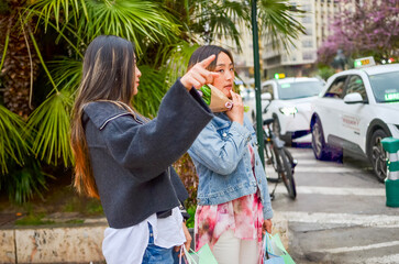 Obraz premium Two young women pointing and holding shopping bags on a city street