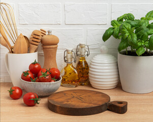Kitchen countertop with cutting board, tomatoes, spices, and basil plant