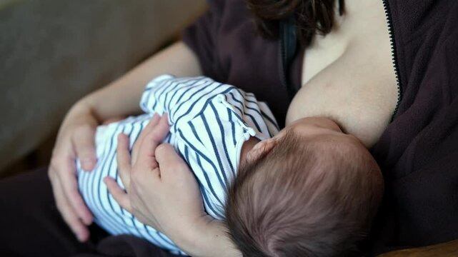 Happy first time asian mom feeding her new baby boy with breast milk is talking and touching him with tenderness. 