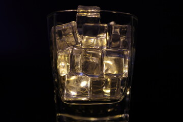 Opaque transparent ice filled drink short glass yellow tungsten light flame smoke fog on black background